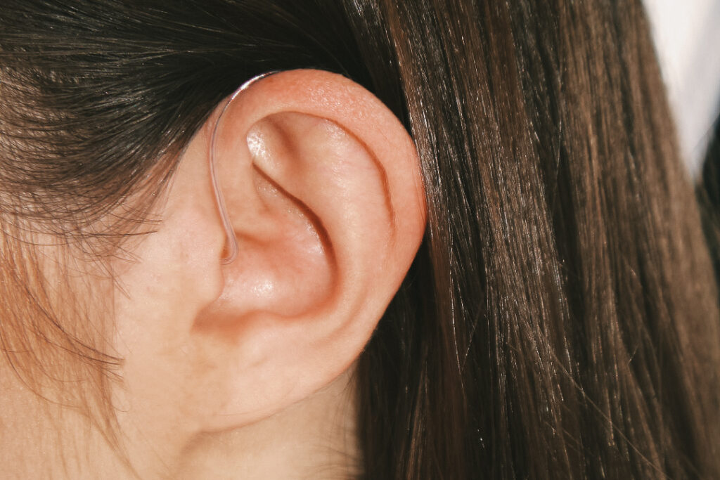 A white woman with brown hair wears a behind-the-ear Lexie hearing aid