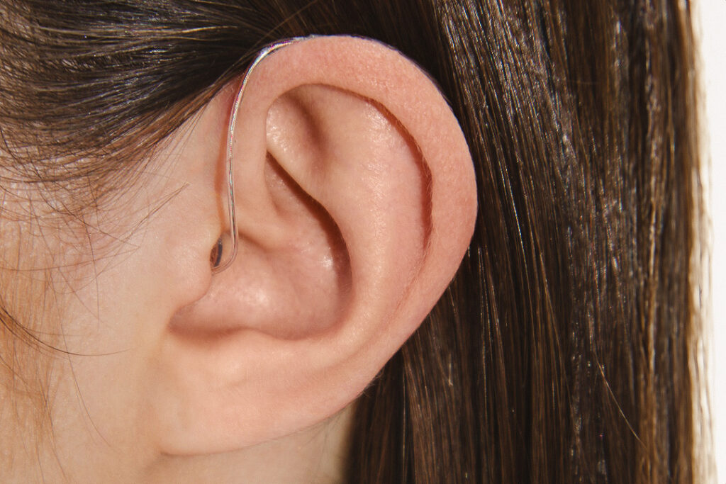 A white woman with brown hair wears an Oticon hearing aid